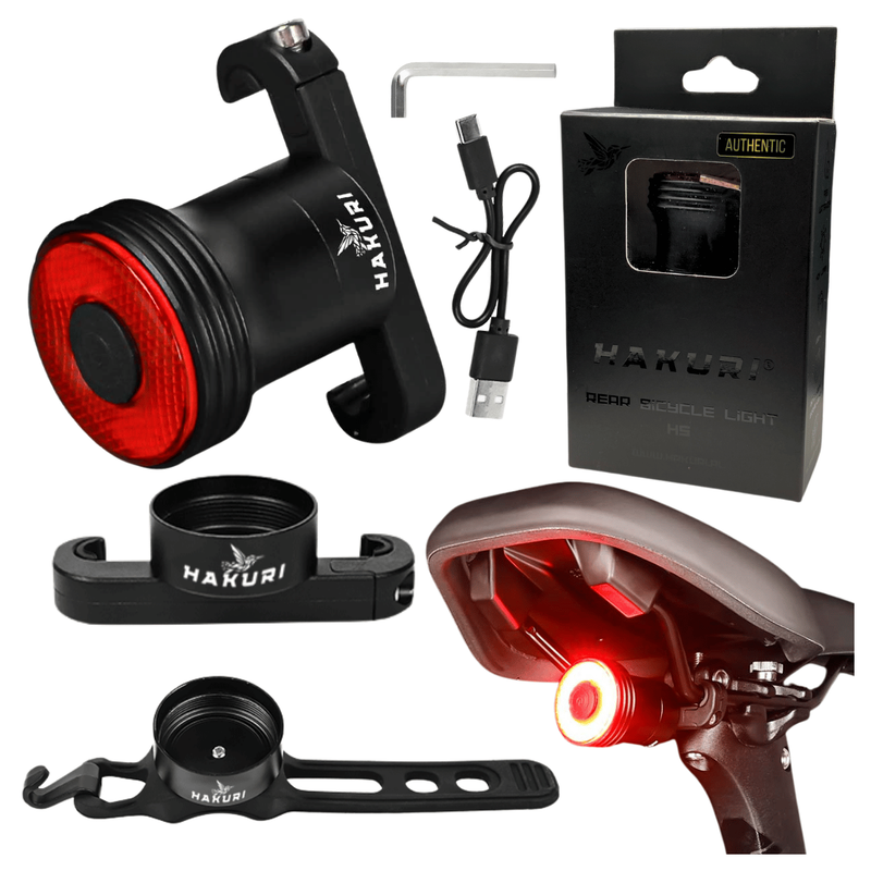Na obrazie widoczna jest tylna lampka rowerowa z czerwonym światłem, zestaw montażowy, kabel USB oraz opakowanie z napisem \'HAKURI REAR BICYCLE LIGHT\'.