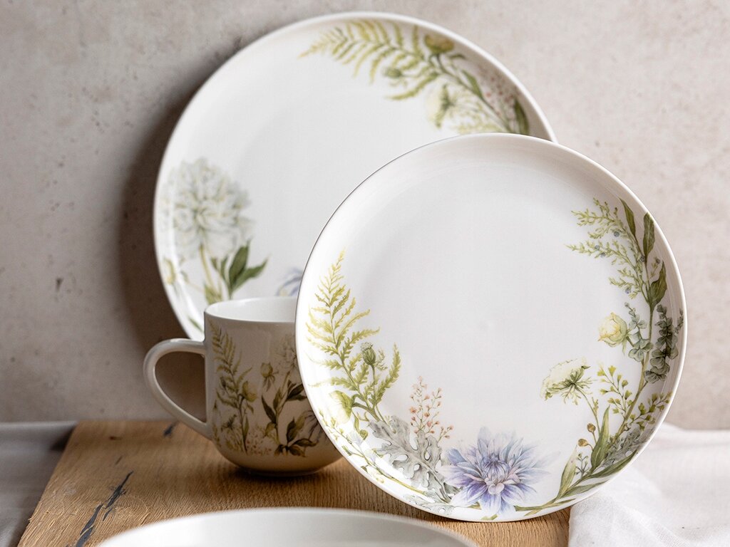 Na obrazie widoczne są dwa talerze i filiżanka z kwiatowym wzorem. Talerze mają elegancki, boho styl z motywami roślinnymi na białym tle.