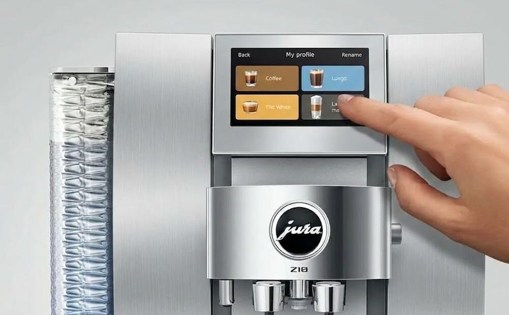 Ekspres do kawy z wyświetlaczem dotykowym, na którym widoczne są opcje: Coffee, Lungo, The Winter, Latte macchiato. Logo \'jura\' znajduje się na froncie urządzenia.