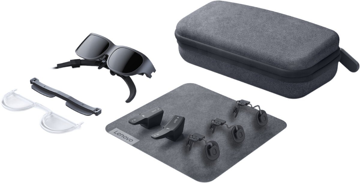 Na obrazie widoczne są okulary przeciwsłoneczne, przezroczyste soczewki, etui oraz kilka małych akcesoriów na szarej macie z logo Lenovo.