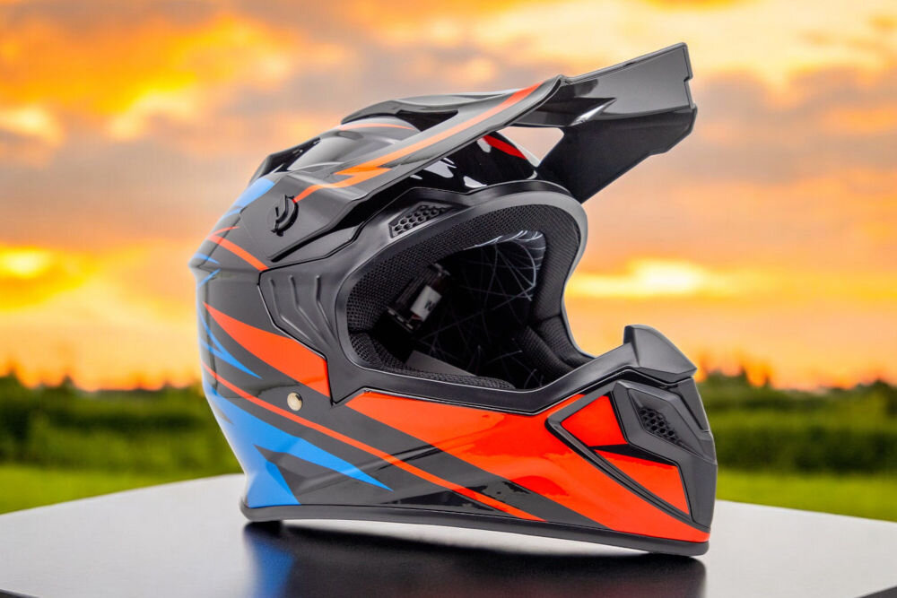 Kask motocyklowy w kolorach czarno-niebieskim z pomarańczowymi akcentami, umieszczony na tle zachodzącego słońca. Kask ma aerodynamiczny kształt z daszkiem i otworami wentylacyjnymi.