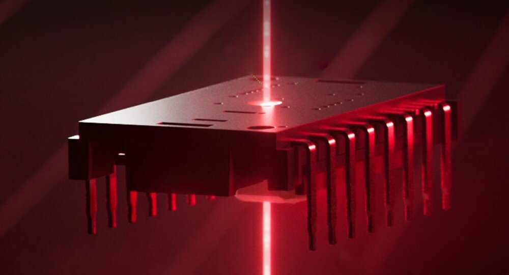 Obraz przedstawia mikroprocesor oświetlony czerwonym światłem laserowym, z widocznymi pinami po bokach. Tło jest ciemne, co podkreśla efekt świetlny.