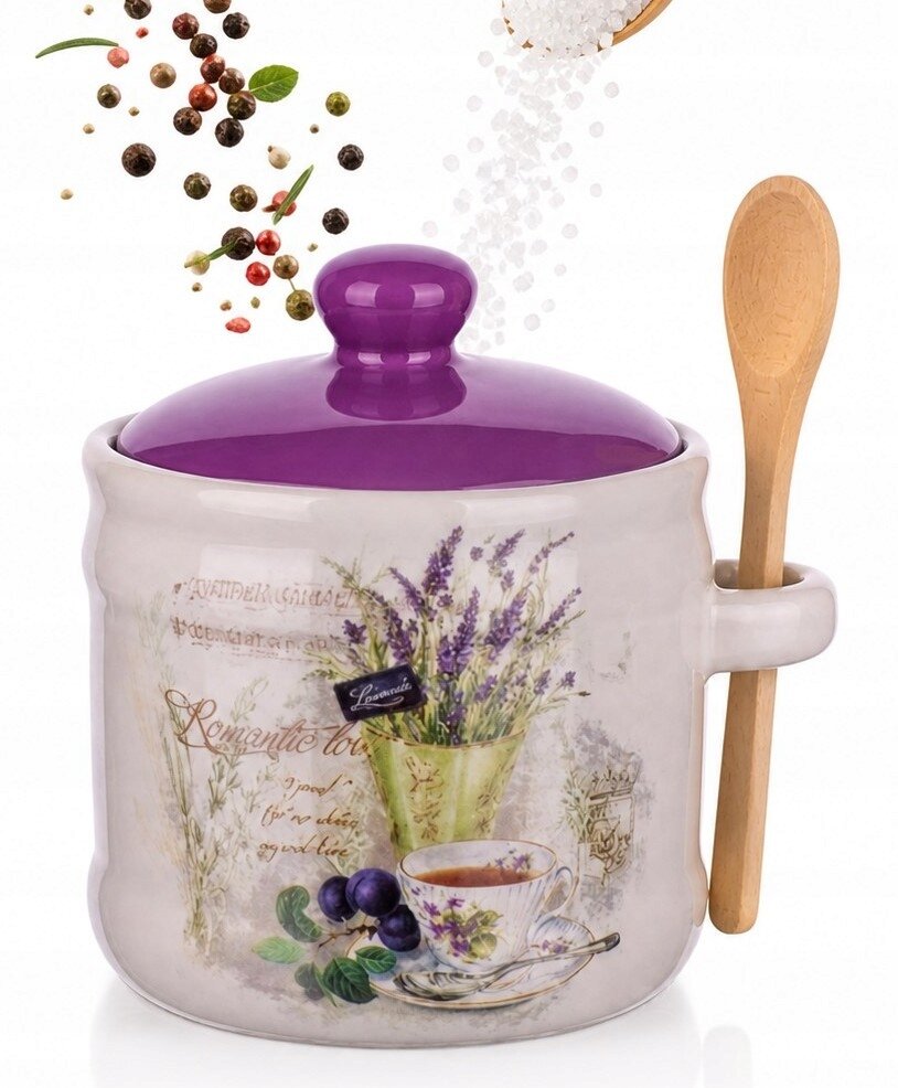Ceramiczny pojemnik z fioletową pokrywką i drewnianą łyżeczką, ozdobiony motywem lawendy, filiżanką i owocami. W tle unoszą się przyprawy i sól.