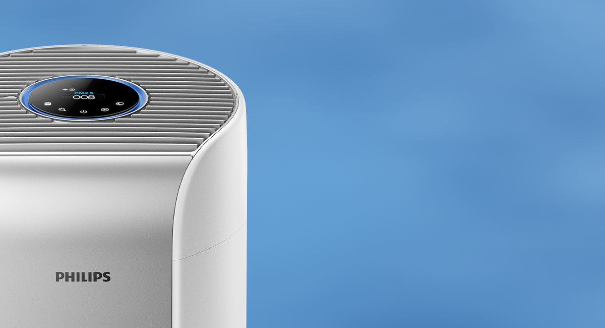 Na obrazie widoczny jest fragment oczyszczacza powietrza z logo PHILIPS. Na górze urządzenia znajduje się okrągły panel sterowania z wyświetlaczem cyfrowym.
