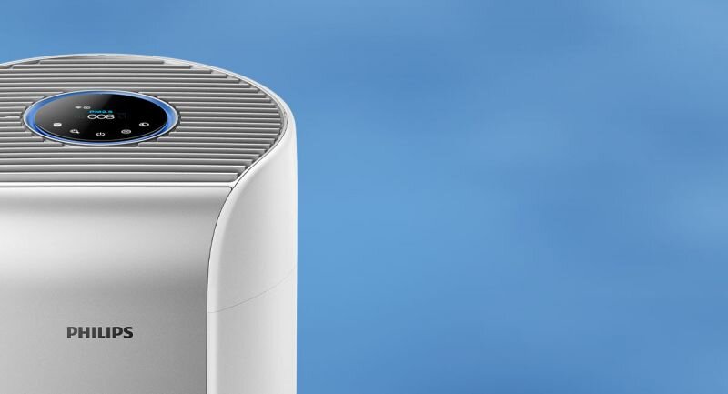 Na obrazie widoczny jest biały oczyszczacz powietrza z logo PHILIPS. Na górze urządzenia znajduje się okrągły panel sterowania z wyświetlaczem cyfrowym.