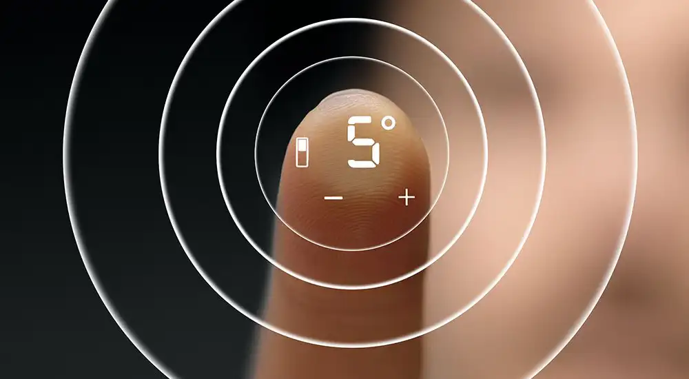 Palec dotyka ekranu dotykowego z wyświetlaczem pokazującym \'5°\' oraz ikonami baterii, minusa i plusa. W tle widoczne są koncentryczne okręgi.