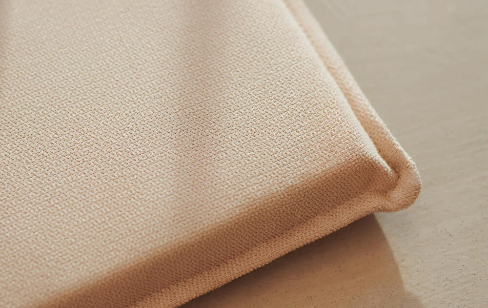 Zbliżenie na beżowy materiał o teksturowanej powierzchni, prawdopodobnie fragment poduszki.