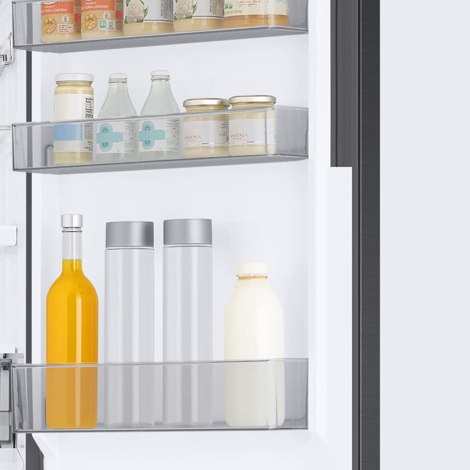Wnętrze lodówki z trzema półkami na drzwiach, na których znajdują się różne produkty spożywcze w słoikach, butelkach i kartonach. Widoczne są m.in. butelki z napojami, słoiki z przetworami oraz kartony z mlekiem.