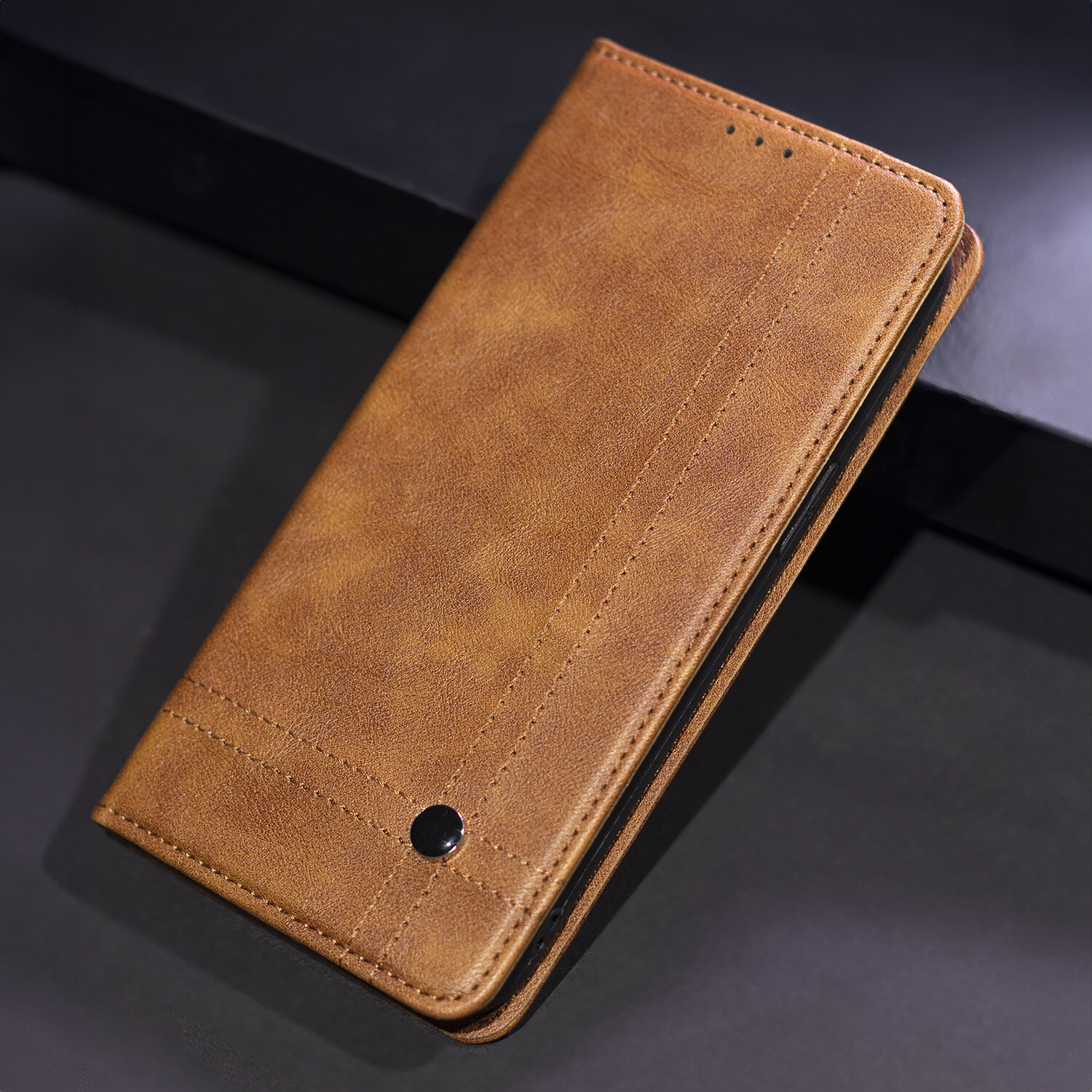 Brązowe etui na telefon z widocznymi przeszyciami i małym, okrągłym elementem dekoracyjnym. Etui jest zamknięte i leży na ciemnym tle.