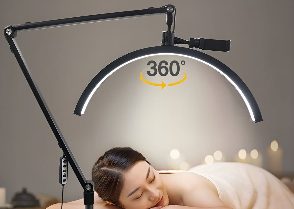 Czarna lampa LED w kształcie łuku z możliwością obrotu o 360 stopni, zamontowana na regulowanym ramieniu. W tle widoczne są zapalone świece i osoba leżąca na plecach.