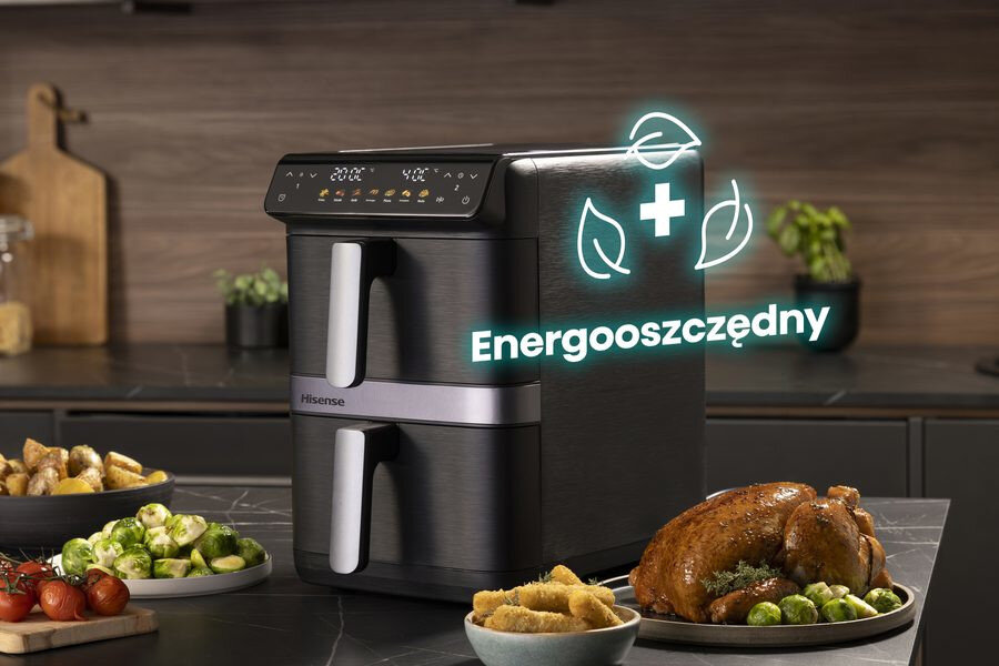 Na blacie kuchennym stoi frytkownica beztłuszczowa z dwoma szufladami, obok której znajdują się talerze z jedzeniem. Na urządzeniu widoczny jest napis \'Energooszczędny\'.