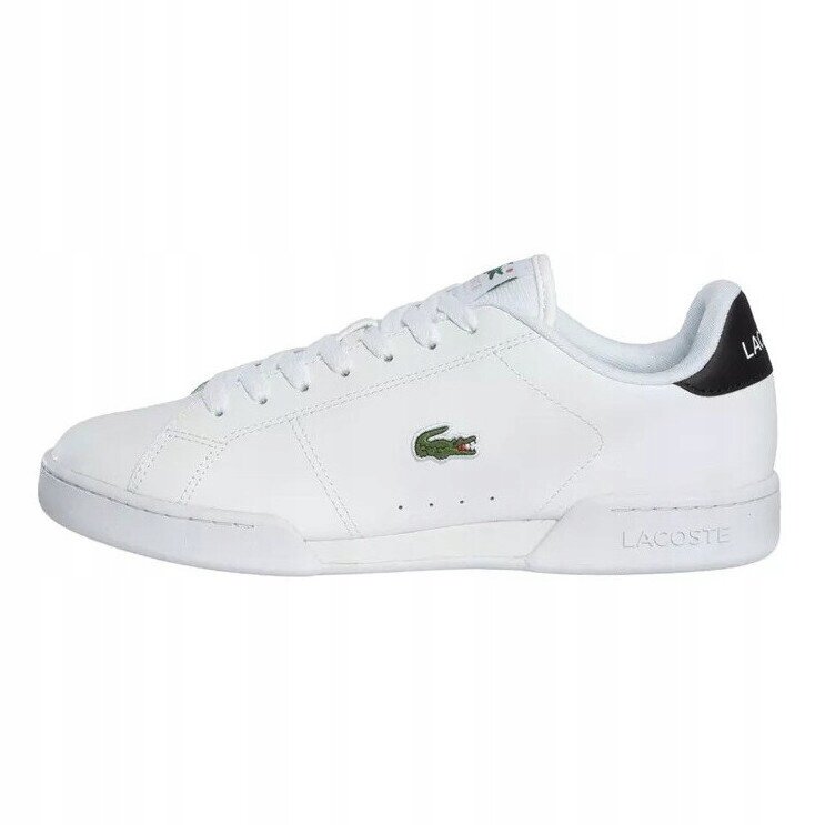 Białe skórzane trampki z logo krokodyla na boku i napisem \'LACOSTE\' na pięcie. Buty mają klasyczny design z białymi sznurówkami.