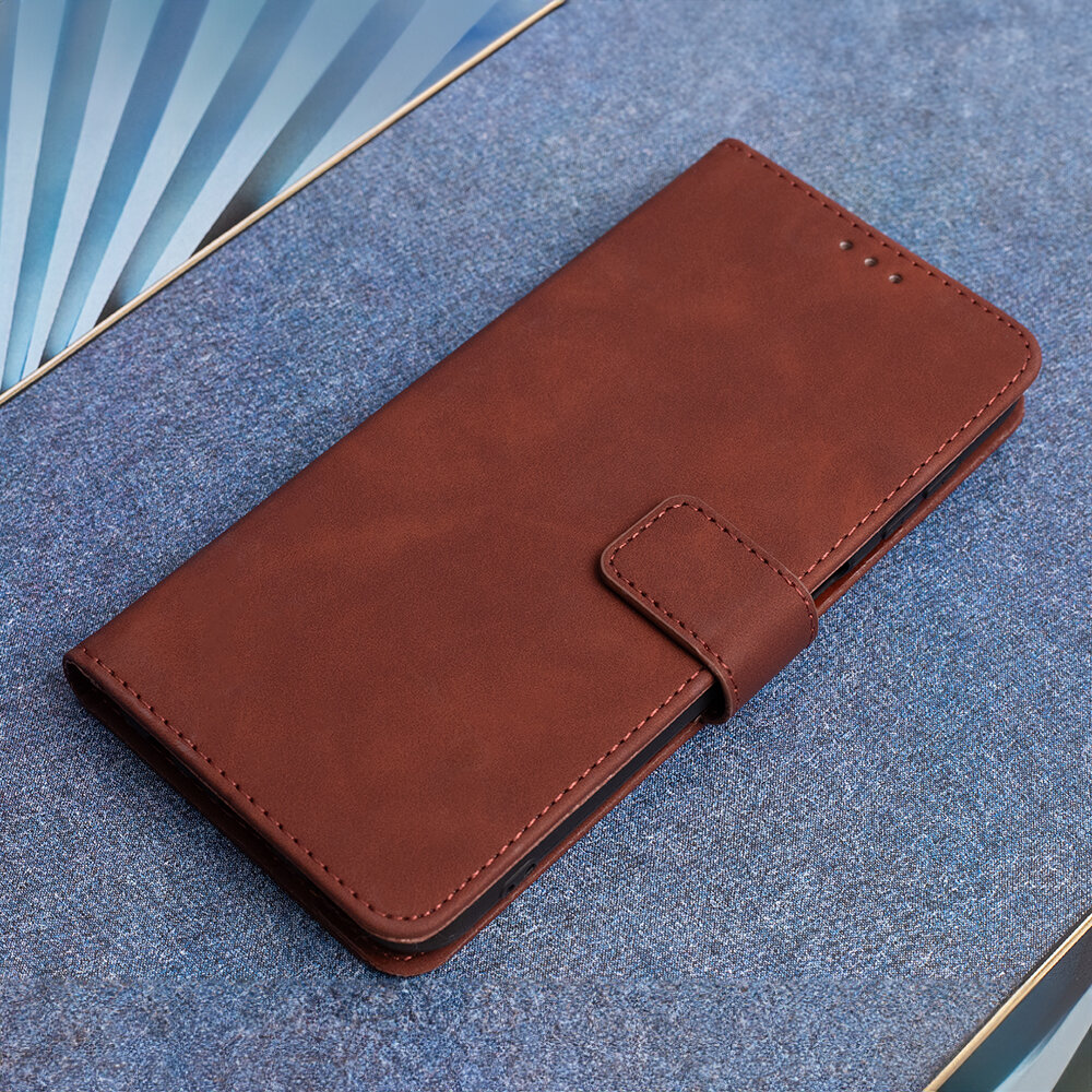 Brązowe etui na telefon leży na niebieskiej powierzchni. Etui ma zapięcie na pasek i widoczne przeszycia na krawędziach.
