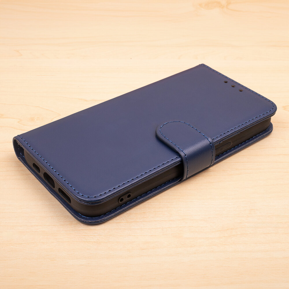 Granatowe etui na telefon leży na drewnianej powierzchni. Etui ma zamknięcie na magnes i otwory na porty urządzenia.