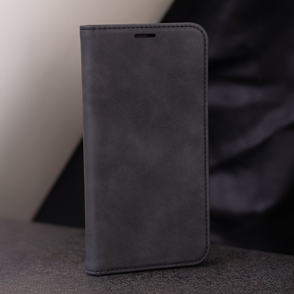 Czarne etui na telefon wykonane z materiału przypominającego zamsz, ustawione pionowo na powierzchni. Tło jest rozmyte i ciemne.