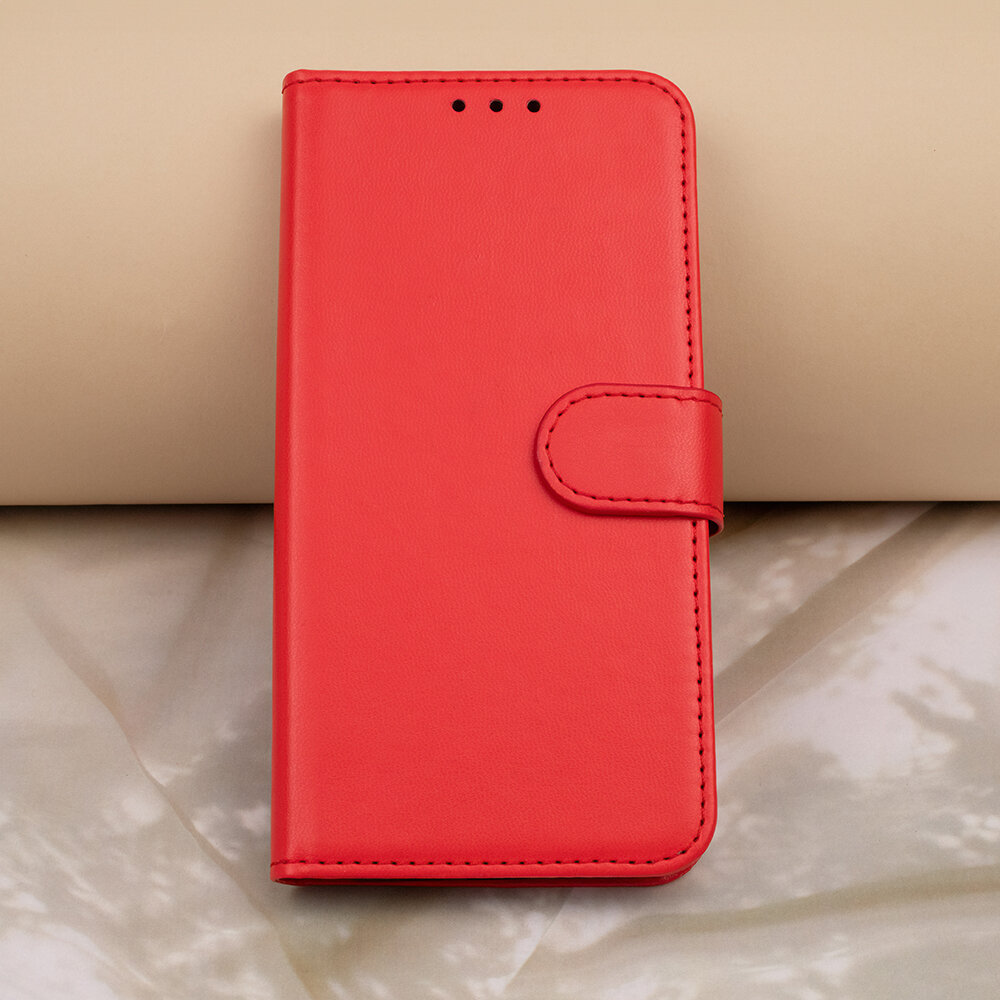 Czerwone etui na telefon z klapką, wykonane z gładkiego materiału, z trzema małymi otworami na górze. Etui posiada zapięcie na pasek z zatrzaskiem.