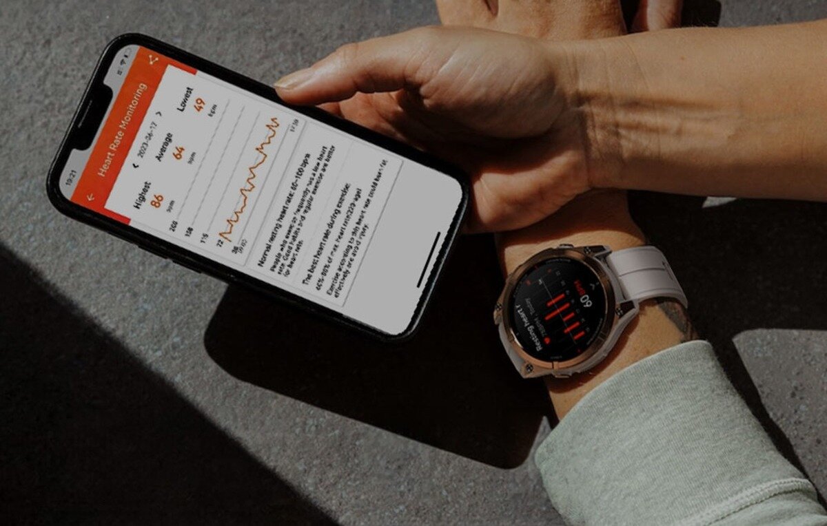 Osoba trzyma smartfon z aplikacją pokazującą dane dotyczące tętna, a na nadgarstku ma założony smartwatch z wyświetlaczem pokazującym podobne informacje. Smartwatch ma czarny ekran z czerwonymi i białymi elementami graficznymi.