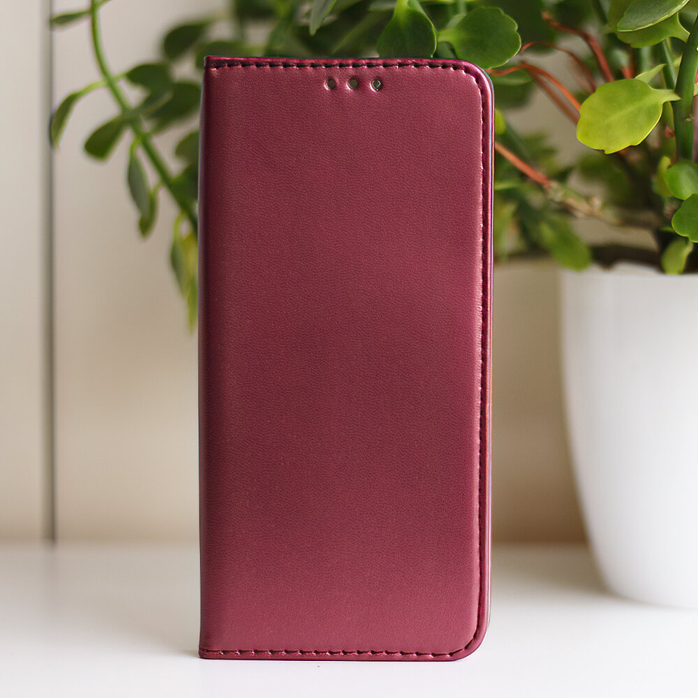 Burgundowe etui na telefon z klapką, ustawione pionowo na tle rośliny w doniczce.