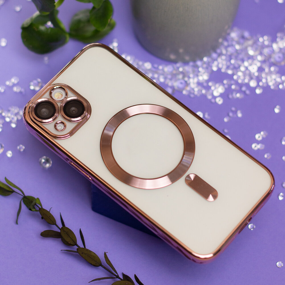 Etui na telefon w kolorze różowo-złotym z okrągłym metalicznym elementem na tylnej części. W tle widoczne są dekoracyjne liście i błyszczące elementy na fioletowym tle.