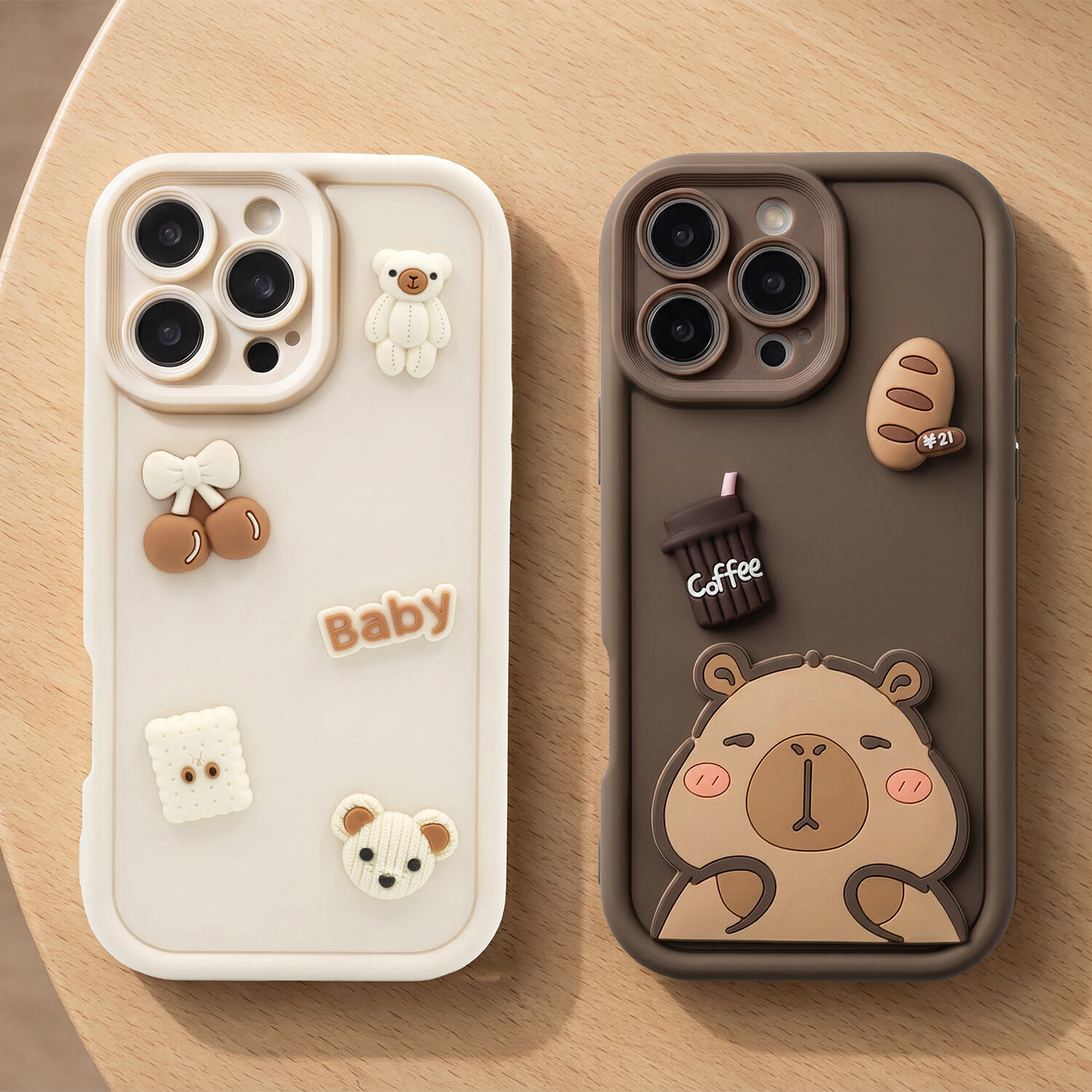 Dwa etui na telefon z motywem misia, jedno w kolorze kremowym z napisem \'Baby\' i ozdobami, drugie brązowe z napisem \'Coffee\' i grafiką misia. Oba etui mają wycięcia na aparat z trzema obiektywami.