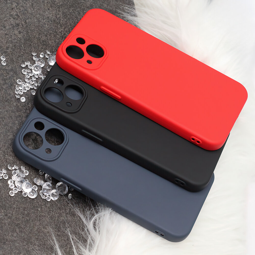 Na obrazie widoczne są trzy silikonowe etui na telefon w kolorach czerwonym, czarnym i granatowym, ułożone jedno na drugim. Obok etui znajdują się małe, przezroczyste kryształki na szarej powierzchni.