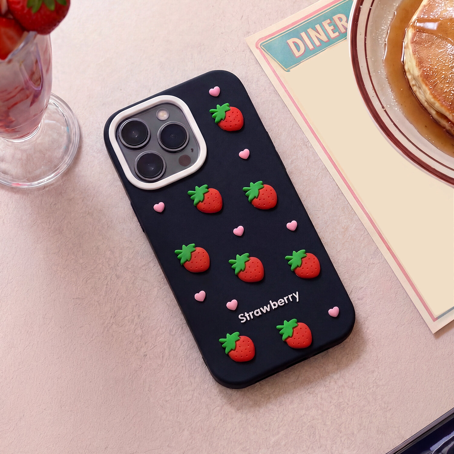 Czarna nakładka na telefon z motywem truskawek i małych różowych serduszek, z napisem \'Strawberry\'.