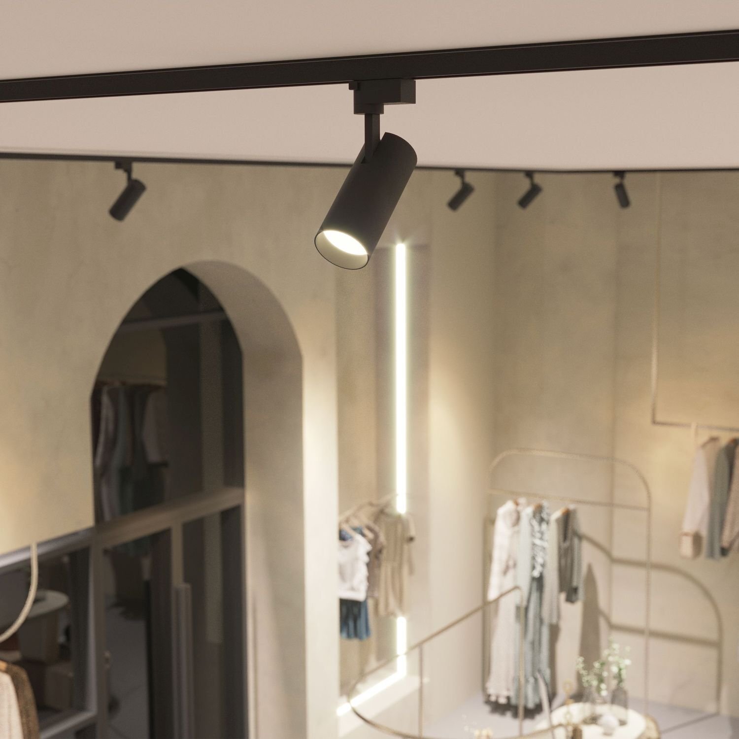 Wnętrze sklepu z widocznym reflektorem szynowym zamontowanym na suficie. W tle widać ubrania wiszące na wieszakach oraz elementy dekoracyjne.