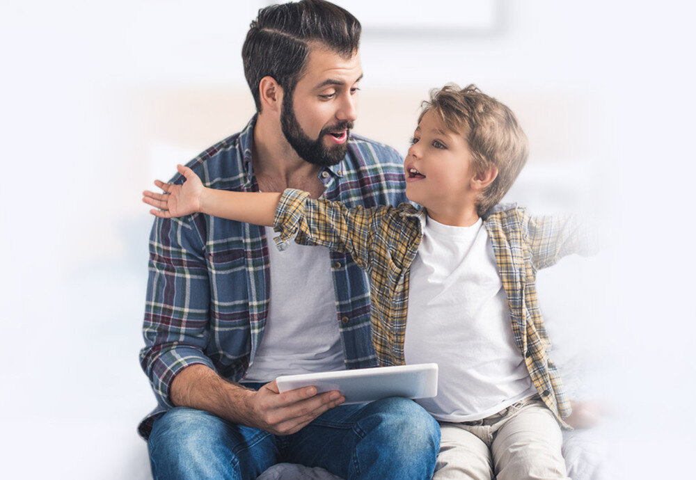 Na obrazie widać dwie osoby siedzące na kanapie, jedna z nich trzyma tablet. Obie osoby są ubrane w koszule w kratę i wyglądają na zadowolone.