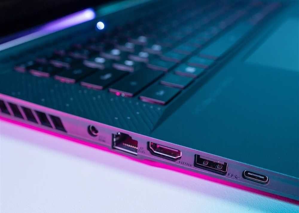Zbliżenie na boczną krawędź laptopa z widocznymi portami: Ethernet, HDMI, USB i USB-C. Obudowa ma metaliczne wykończenie z różowym podświetleniem.