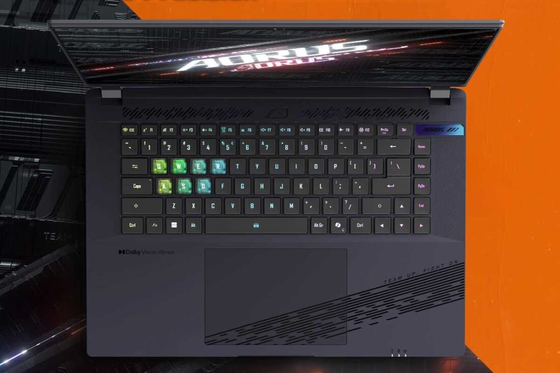 Laptop z otwartą pokrywą, na której widnieje napis \'AORUS\'. Klawiatura podświetlana w różnych kolorach, z widocznym logo \'Dolby Vision Atmos\'.
