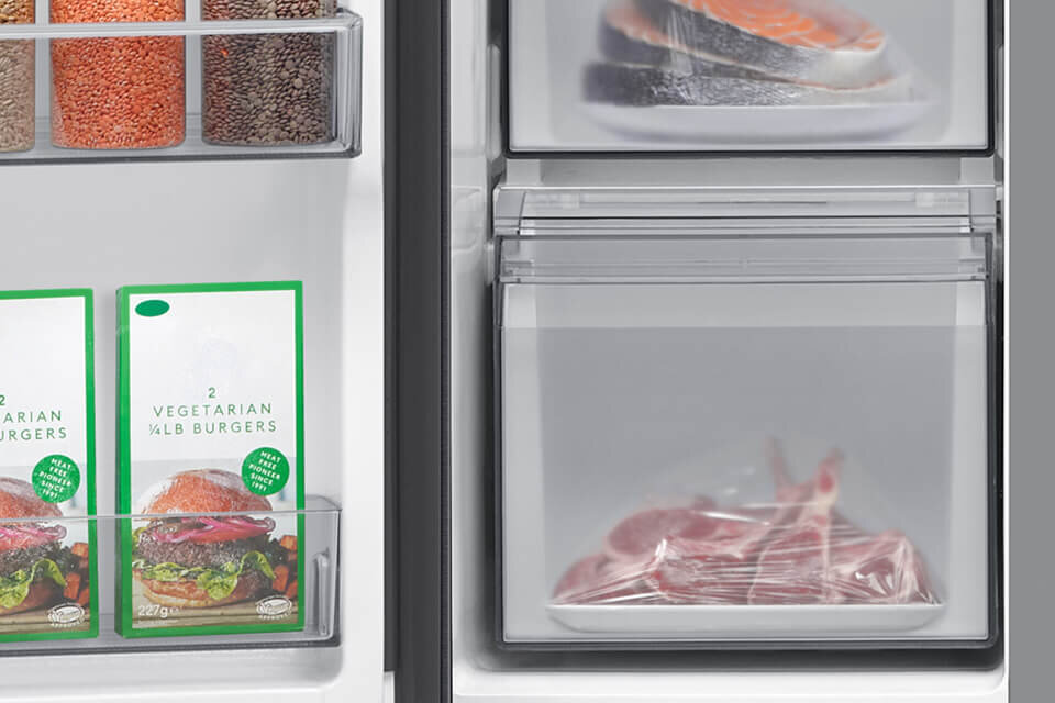 Wnętrze lodówki z widocznymi produktami spożywczymi, w tym opakowaniami z napisem \'2 VEGETARIAN 1/4LB BURGERS\'. Obok znajdują się przezroczyste szuflady z zapakowanymi kawałkami mięsa i rybą.