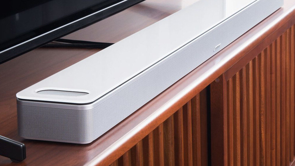 Biały soundbar umieszczony na drewnianej szafce, z widocznym logo \'Bose\' na przedniej części urządzenia.