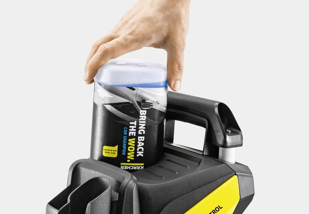 Ręka umieszcza pojemnik z napisem \'BRING BACK THE WOW CAR SHAMPOO\' na urządzeniu z logo KARCHER. Widoczna jest część myjki ciśnieniowej z uchwytem i żółtym elementem.