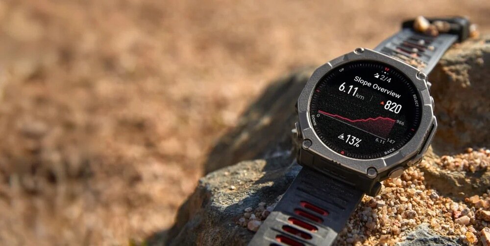Smartwatch z czarno-srebrną kopertą leży na kamieniu, wyświetlając ekran z informacjami: \'Slope Overview\', \'6.11 km\', \'820\', \'43%\'.