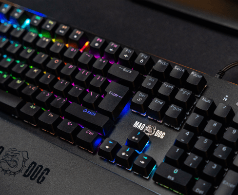 Klawiatura mechaniczna z podświetleniem RGB, widoczne klawisze z oznaczeniami liter i funkcji. Na obudowie znajduje się logo \'MAD DOG\'.