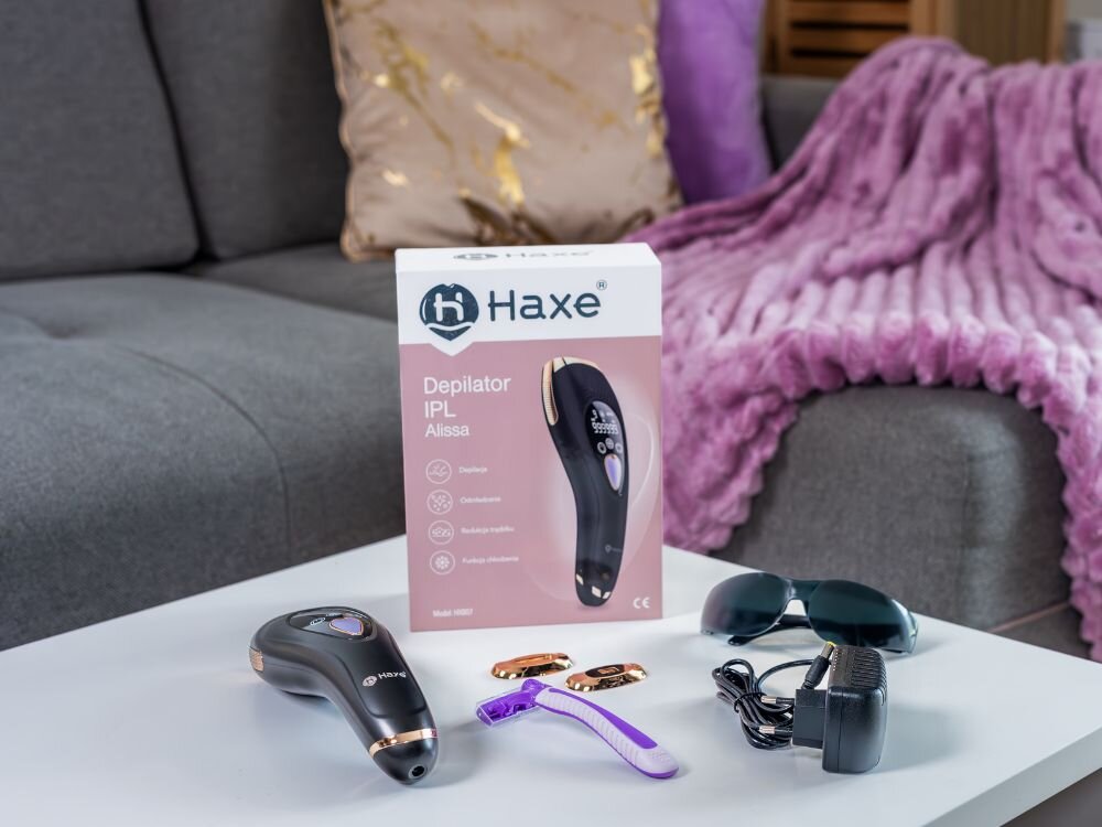 Depilator HAXE IPL Alissa HX807 na zdjęciu widoczny stolik na którym postawione jest oryginalne pudełko obok leży depilator dwie magnetyczne głowice maszynka do golenia okulary ochronne zasilacz sieciowy