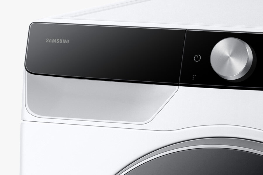 Fragment pralki z widocznym panelem sterowania, na którym znajduje się logo \'SAMSUNG\' oraz srebrne pokrętło. Panel jest czarny z elementami białymi.