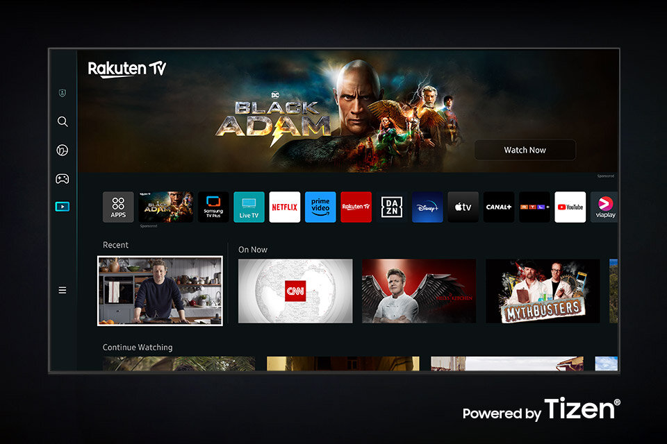 Interfejs telewizora z aplikacjami takimi jak Netflix, Prime Video, YouTube oraz logo \'Rakuten TV\' i \'Powered by Tizen\'. Widoczny jest baner promujący film \'Black Adam\'.