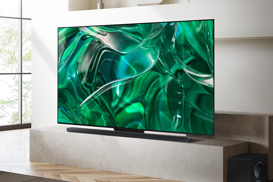 Telewizor z dużym ekranem wyświetlający abstrakcyjny, zielony wzór. Urządzenie stoi na jasnej, nowoczesnej szafce w minimalistycznym wnętrzu.