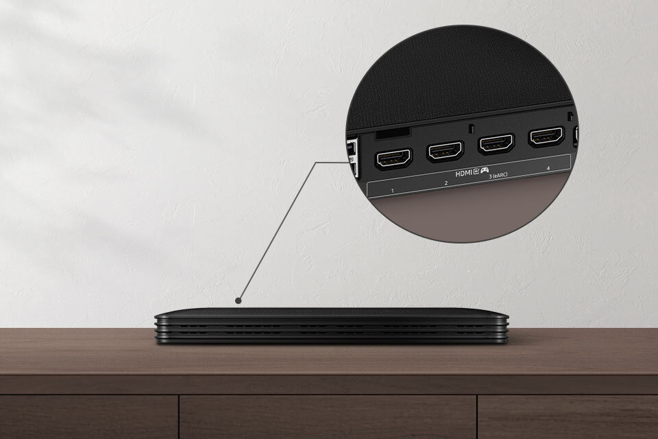 Na drewnianym blacie znajduje się cienkie urządzenie elektroniczne. W powiększeniu pokazano panel z czterema portami HDMI, z których jeden jest oznaczony jako HDMI eARC.