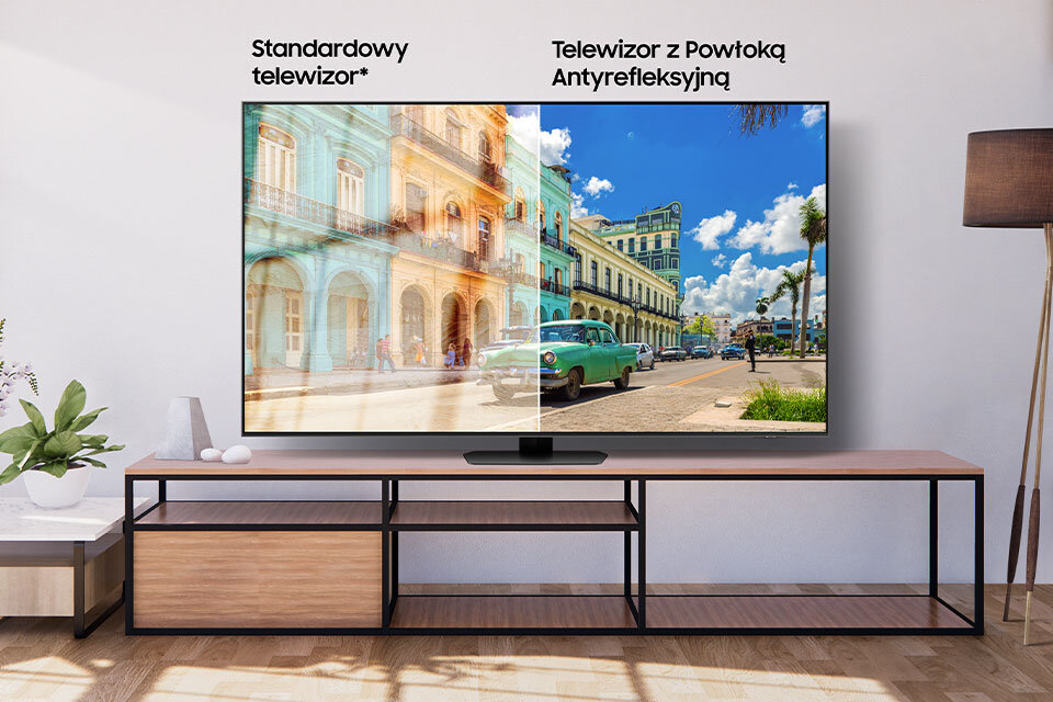 Telewizor pokazuje porównanie obrazu: po lewej stronie \'Standardowy telewizor*\', a po prawej \'Telewizor z Powłoką Antyrefleksyjną\'. Obraz po prawej jest wyraźniejszy i bardziej nasycony kolorami.