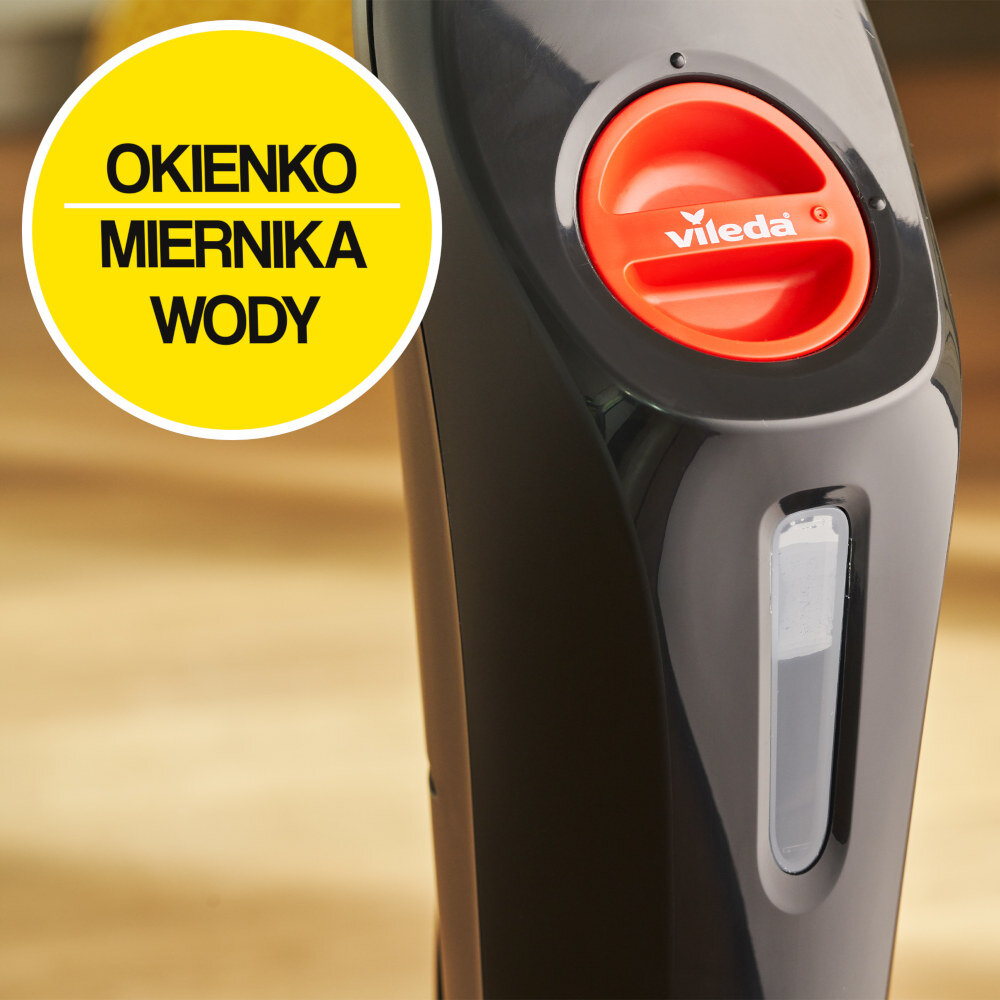 Zbliżenie na czarny mop parowy z czerwonym elementem z logo \'vileda\' oraz okienkiem miernika wody. Na żółtym tle widoczny jest tekst: \'OKIENKO MIERNIKA WODY\'.