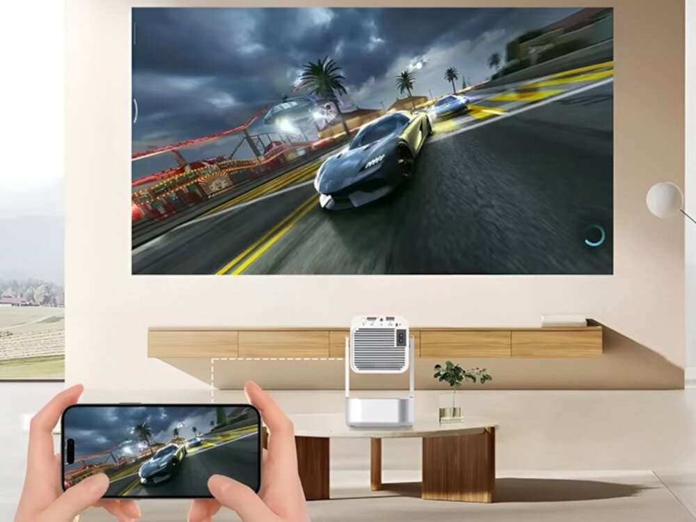Na ścianie wyświetlany jest dynamiczny obraz wyścigu samochodowego, a poniżej znajduje się projektor. Osoba trzyma smartfon, na którym widoczny jest ten sam obraz co na ścianie.