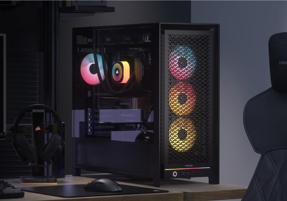 Obudowa komputerowa z trzema podświetlanymi wentylatorami RGB na przednim panelu i przezroczystym panelem bocznym. Na biurku obok znajduje się myszka, podkładka oraz stojak na słuchawki.