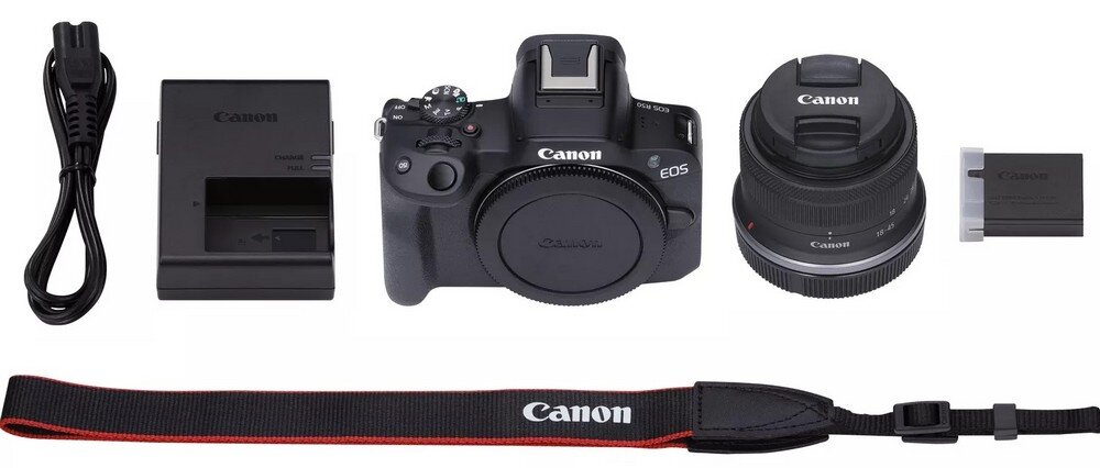Zestaw zawiera aparat bezlusterkowy z logo Canon, obiektyw, ładowarkę, kabel zasilający, baterię oraz pasek z napisem Canon.