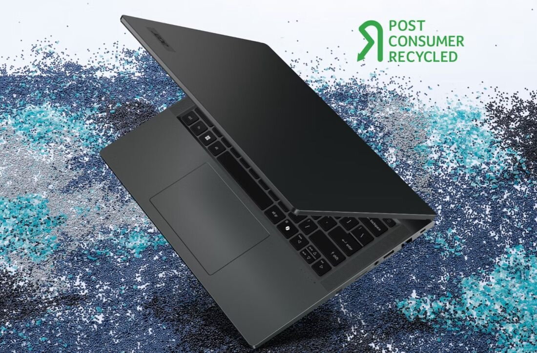 Na obrazie widać otwarty laptop na tle kolorowych drobinek. W prawym górnym rogu znajduje się napis \'POST CONSUMER RECYCLED\'.