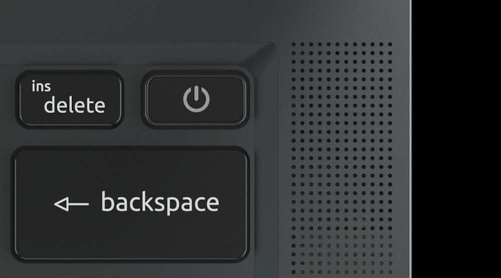 Obraz przedstawia klawiaturę z widocznymi klawiszami: \'ins delete\', przycisk z symbolem zasilania oraz \'backspace\'. Obok klawiszy znajduje się perforowana powierzchnia, prawdopodobnie część obudowy laptopa.