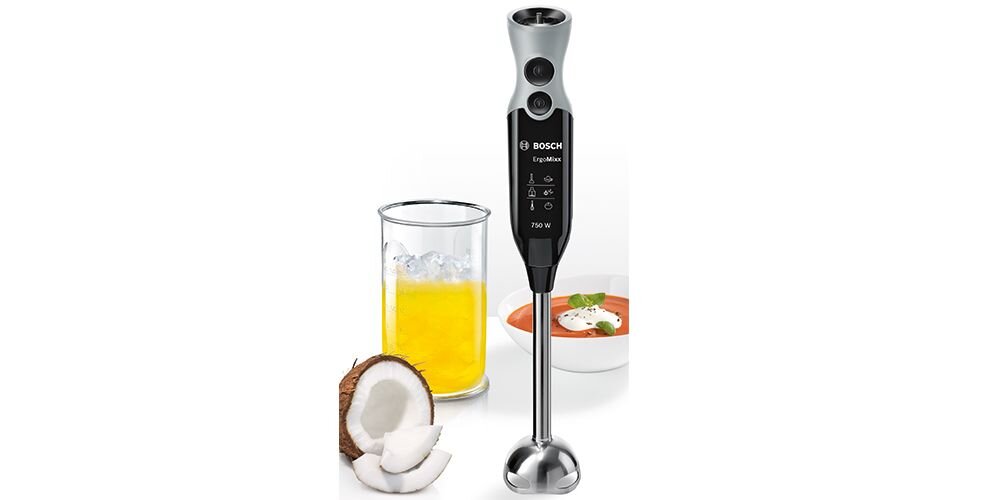Na obrazie znajduje się czarny blender ręczny z metalową stopą, obok którego stoi szklanka z żółtym napojem i połówka kokosa. Na blenderze widoczne jest logo \'Bosch\' oraz napis \'ErgoMixx 750 W\'.