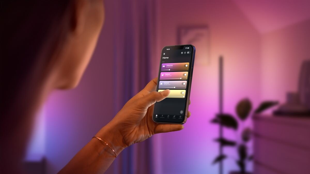 Lampa PHILIPS HUE Play 929004321101 Bluetooth, Zigbee, konfiguracja, Matter, telefon, Bluetooth, Pokój z kolorowym światłem i telefonem w dłoni.