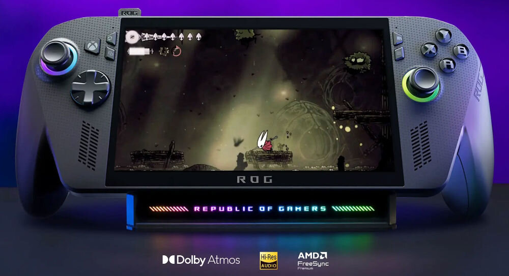 Przenośna konsola do gier z ekranem wyświetlającym grę, z logo \'ROG\' na dole. Na podstawce widnieje napis \'REPUBLIC OF GAMERS\', a poniżej znajdują się logotypy: Dolby Atmos, Hi-Res Audio, AMD FreeSync Premium.